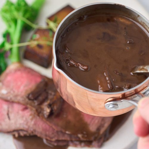 svampesauce med rødvin i lille sovsegryde med tallerken med kød, kartofler og grøntsager.
