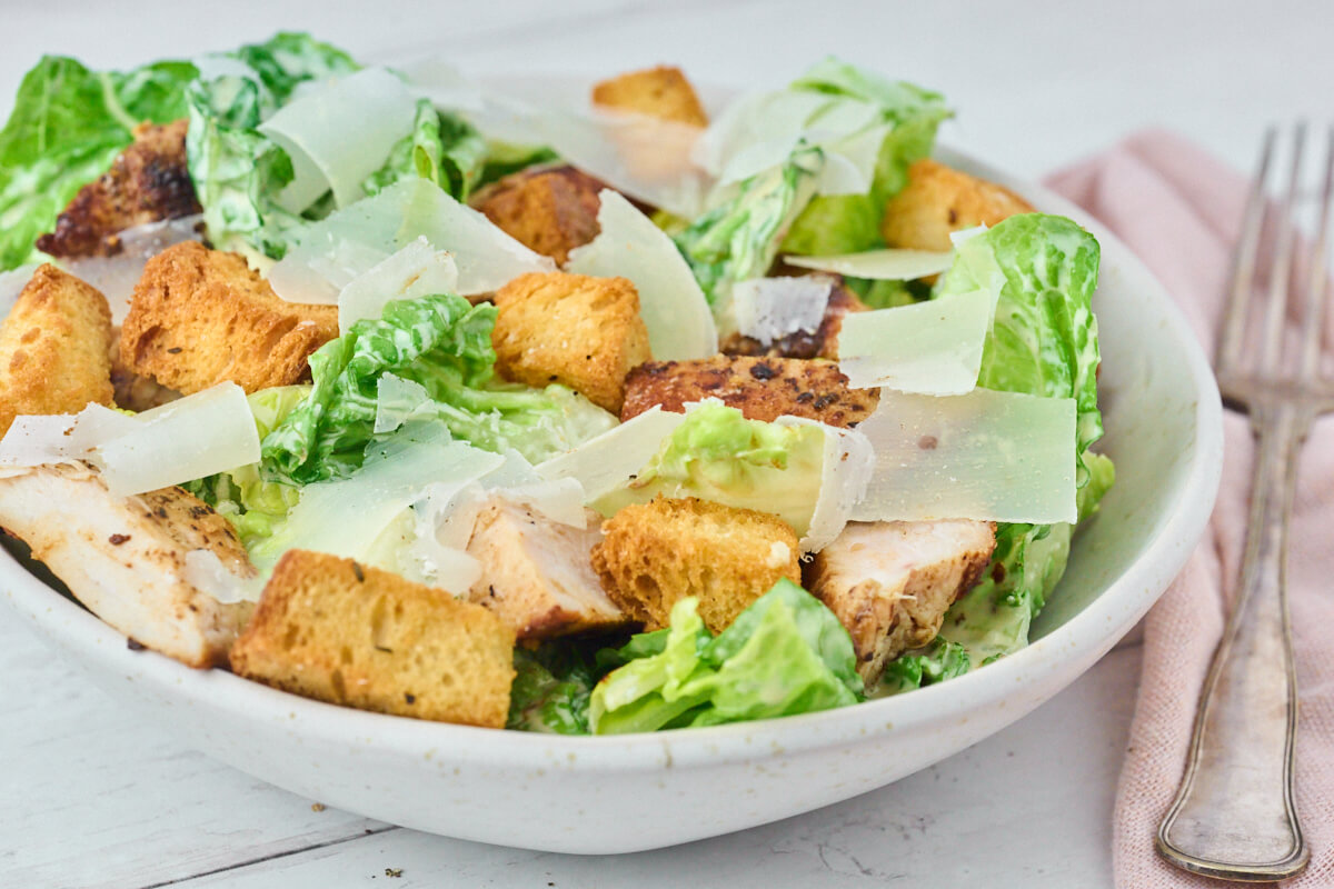 cæsarsalat med kylling, brødcroutoner og parmesan i en skål klar til servering.