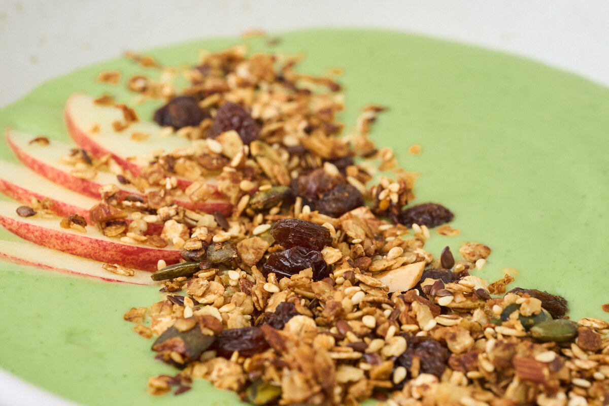 toppen af en grøn smoothie bowl med granola og æble.