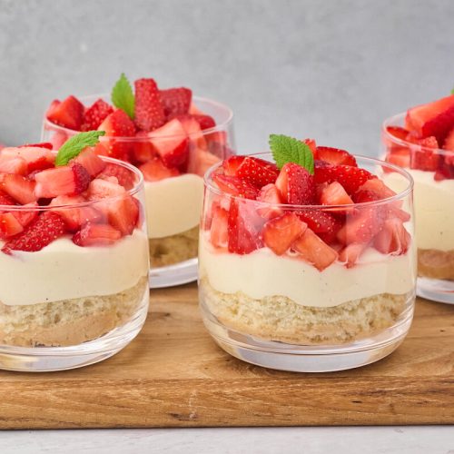 portionsanrettede jordbærkager i glas som små desserter med lagkagebund, creme og marinerede jordbær.