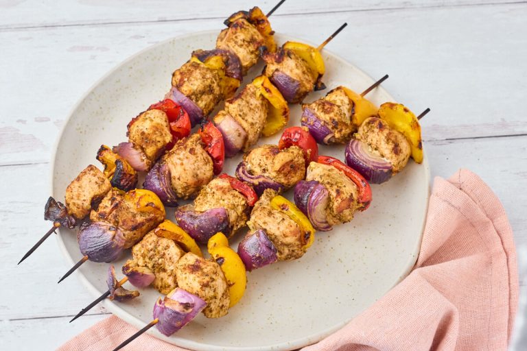 grillspyd med gyrosmarineret kylling og peberfrugt samt rødløg på serveringsfad.