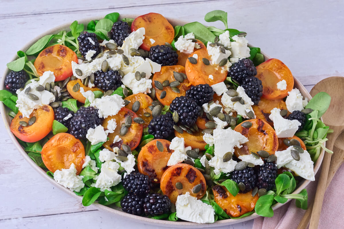 salat med grillede abrikoser, feta og brombær på salatfad.
