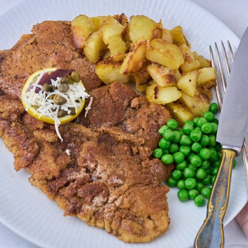 wienerschnitzel med dreng serveret med brasede kartofler, smørsauce og ærter.