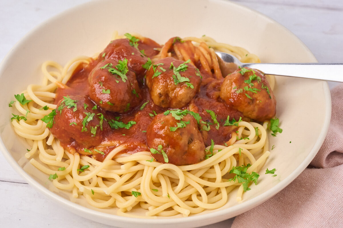 Kyllingekødboller i tomatsovs serveret med spaghetti og frisk persille.