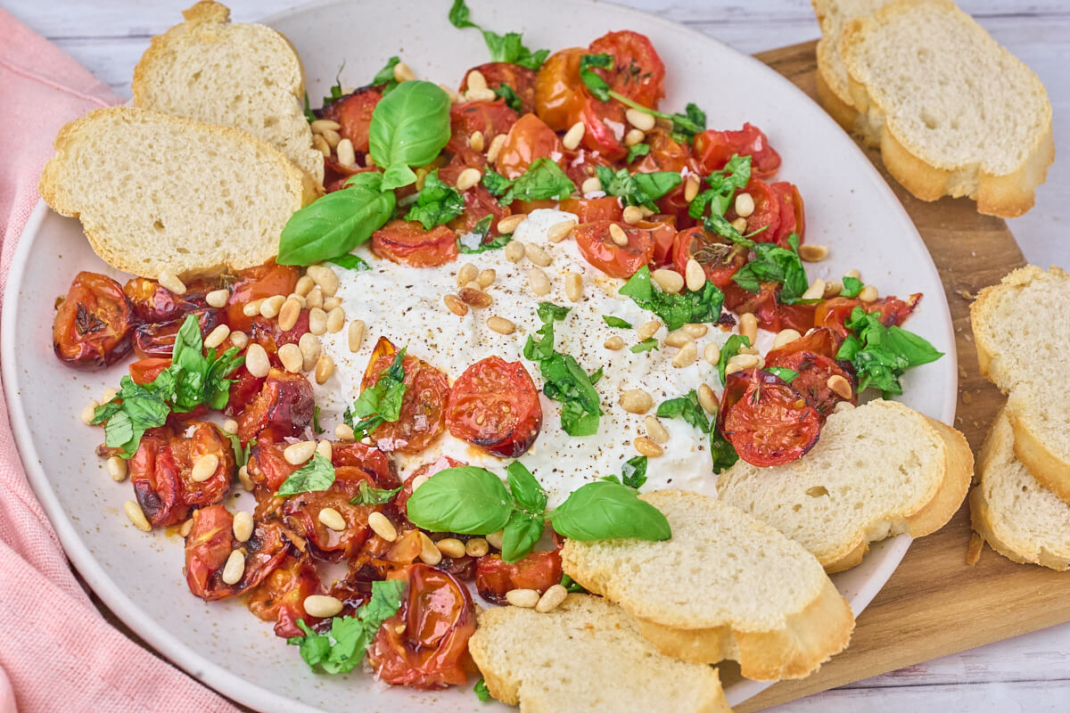Burrata med bagte tomater, pinjekerner og basilikum serveret med brød til.