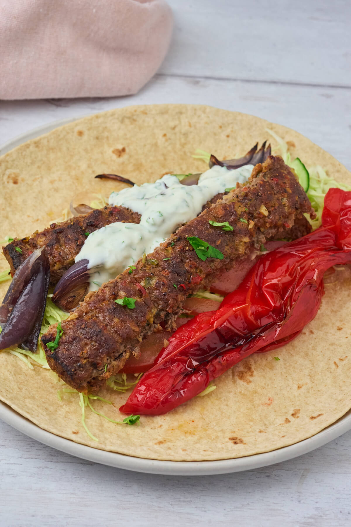 servering af Adana kebab i fladbrød med grønt og dressing.