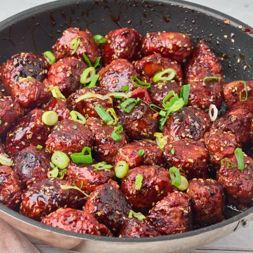 Sticky kyllingefrikadeller med grøntsager i pande med hakkede forårløg på toppen.