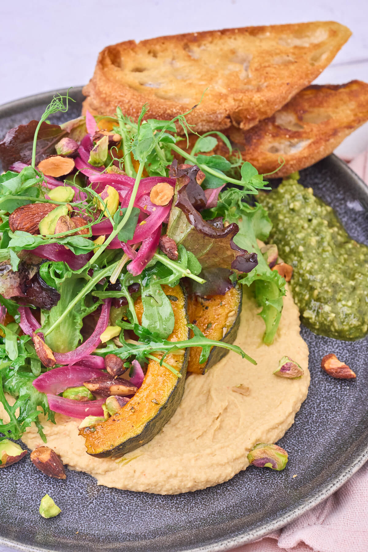 anretning med hummus, bagt grøn hokkaido græskar, grøn salat, knas og brød.