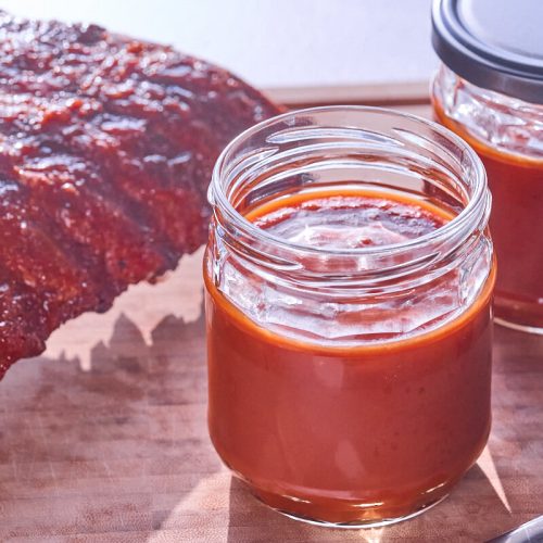 hjemmelavet barbecuesauce med bourbon i glas med spareribs.